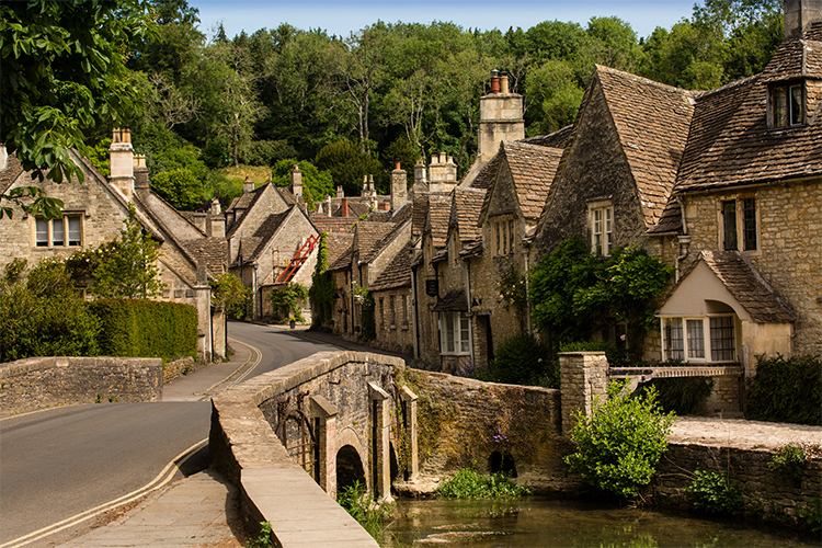 A village within the Cotswolds consisting of traditional houses and a bridge over a stream. style=